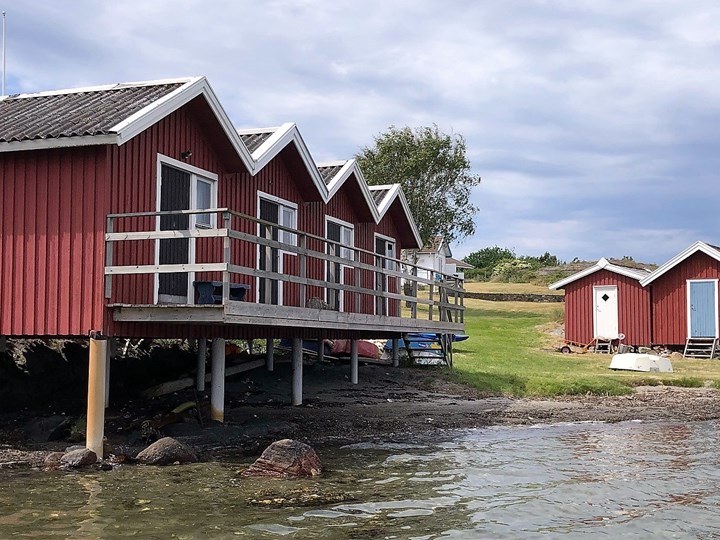 Fyra röda sjöbodar i rad vid strandbrynet