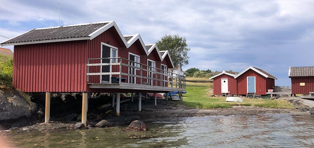 Fyra röda sjöbodar i rad vid strandbrynet